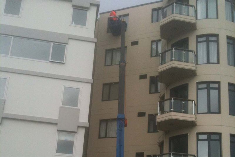 Worker in a cherry picker repairing an upper floor on a beige apartment building.