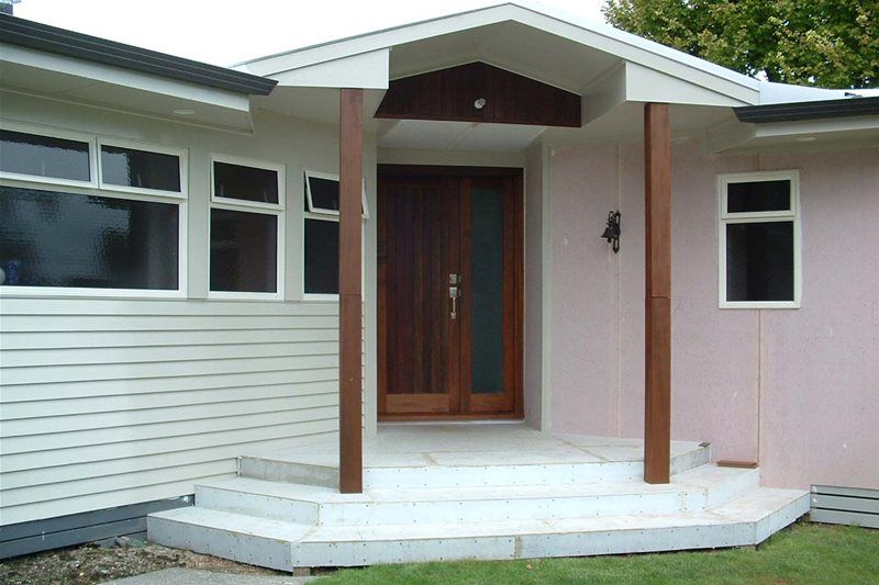 Front entrance of a house with white siding, pink walls, wooden door, and small porch steps.