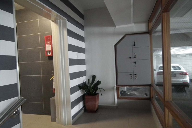 Covered hallway with striped wall, potted plant, and parked car visible through glass