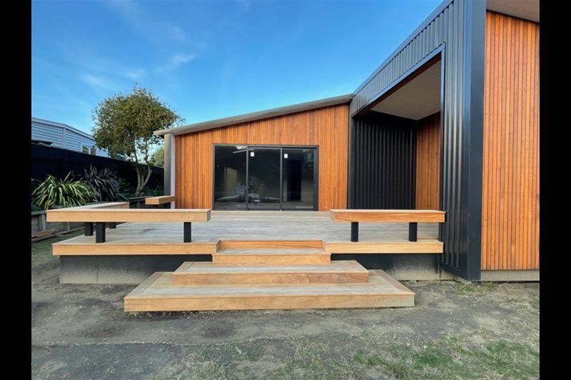Modern wooden house exterior with a front deck and steps under a clear sky