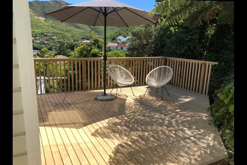 Wooden patio deck with two white chairs and a large umbrella overlooking a green valley.