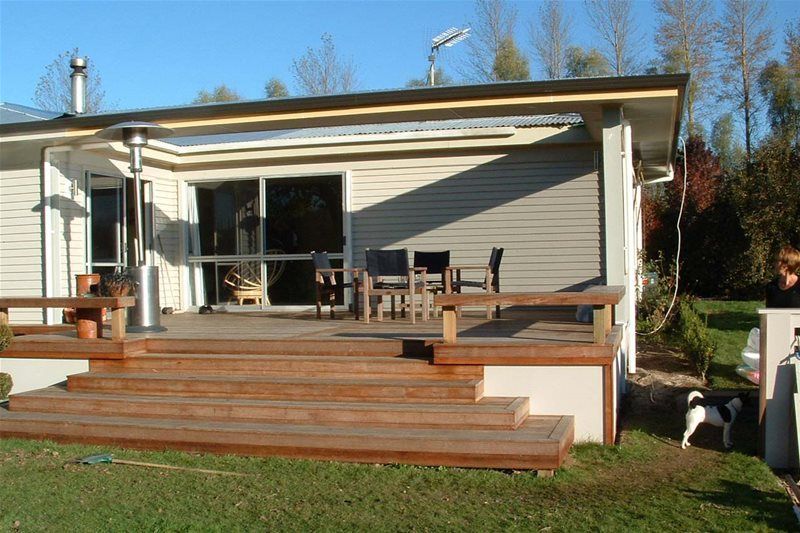 House with a wooden deck and steps leading to a patio in a sunny backyard