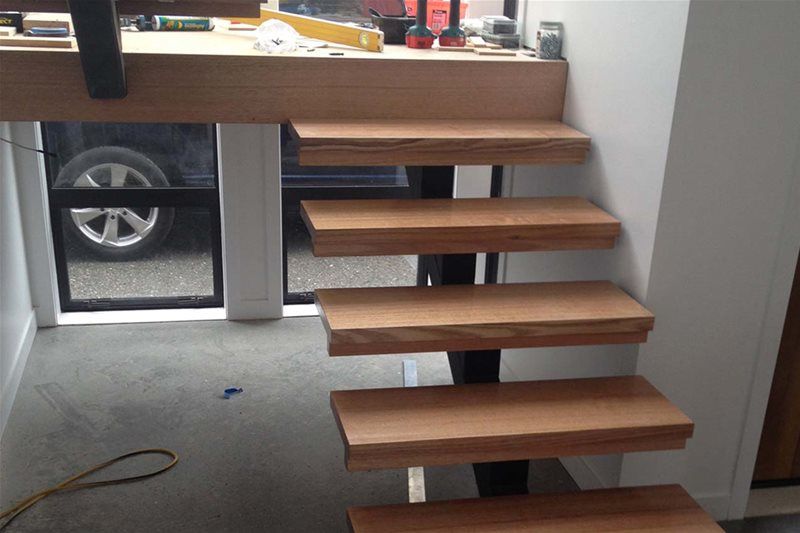 Floating wooden staircase in a modern interior with a car visible through the glass wall