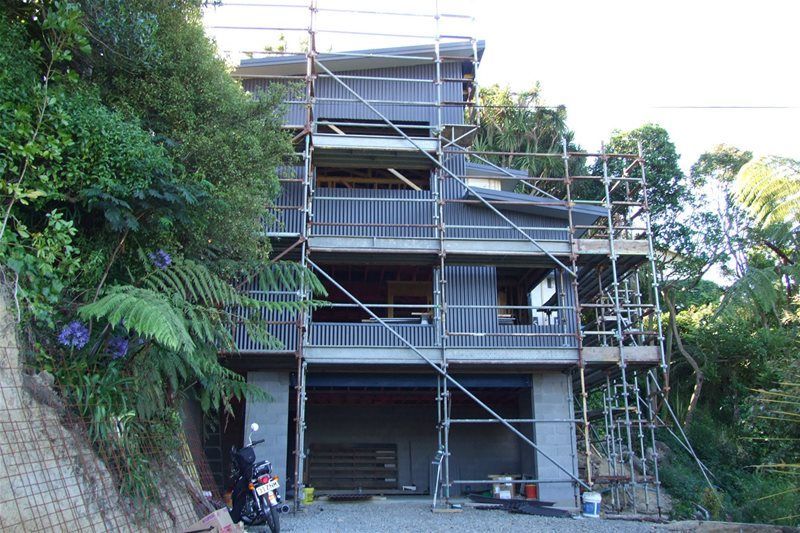Scaffolding surrounds a house under construction beside a wooded hillside.