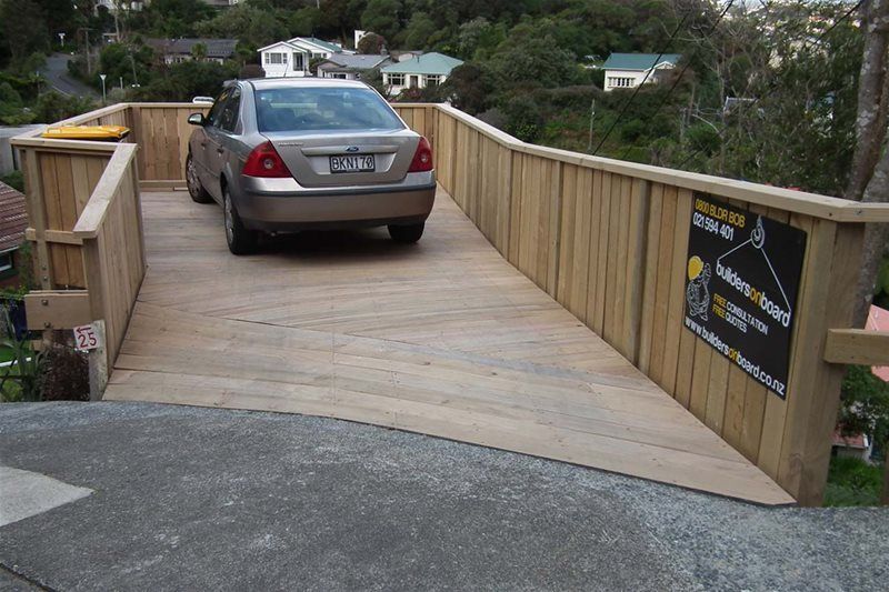 Silver sedan on a wooden ramp with railings, leading to a driveway beside a house