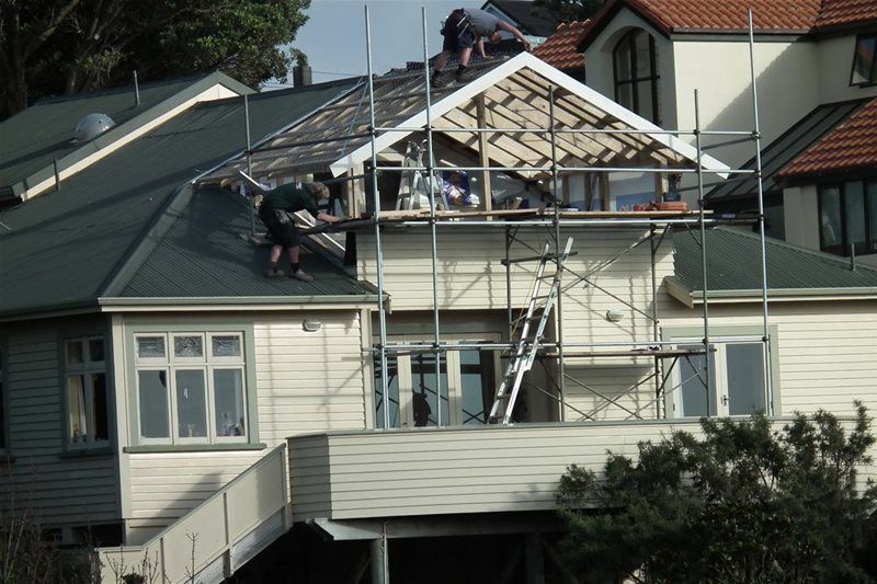 Workers repairing a house roof with scaffolding and ladders under construction.