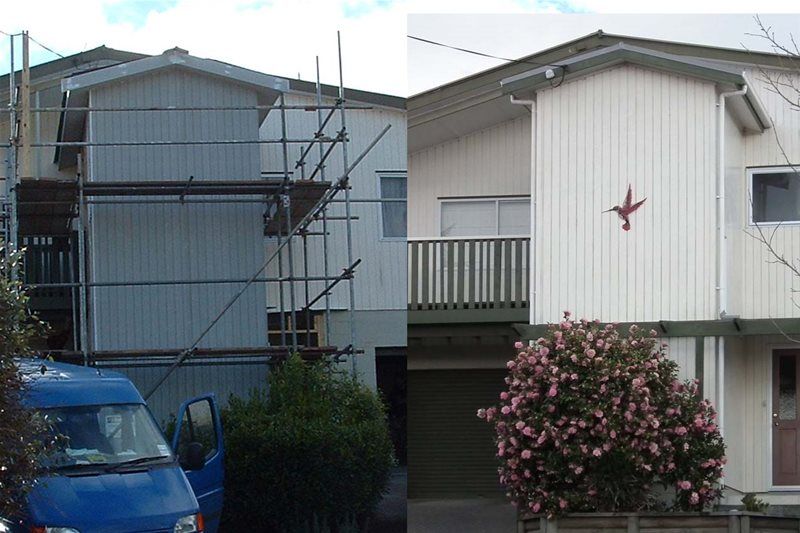 Two small apartment buildings with a blue car, scaffolding, and pink flowering shrubs in front