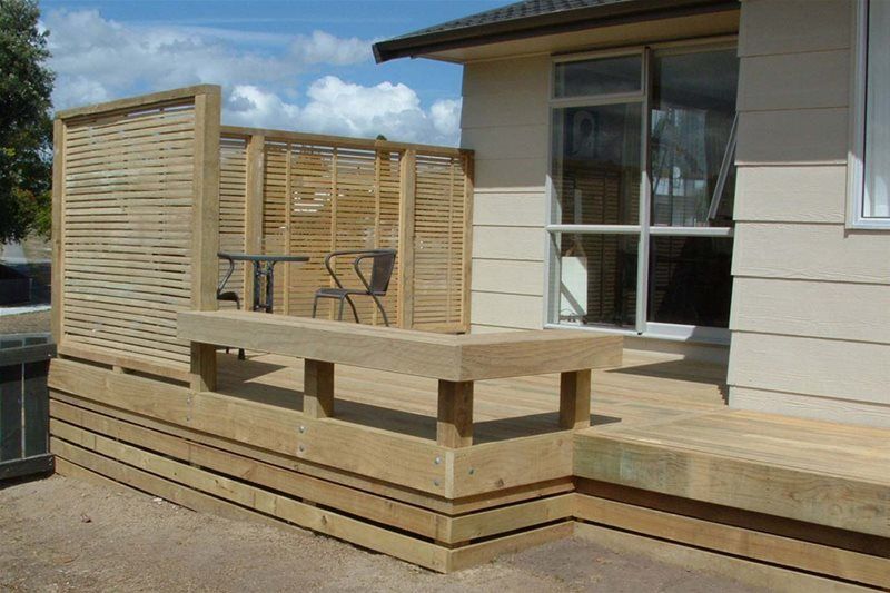 Wooden deck extension with railing beside a house, with a small table and chairs under a partly cloudy sky