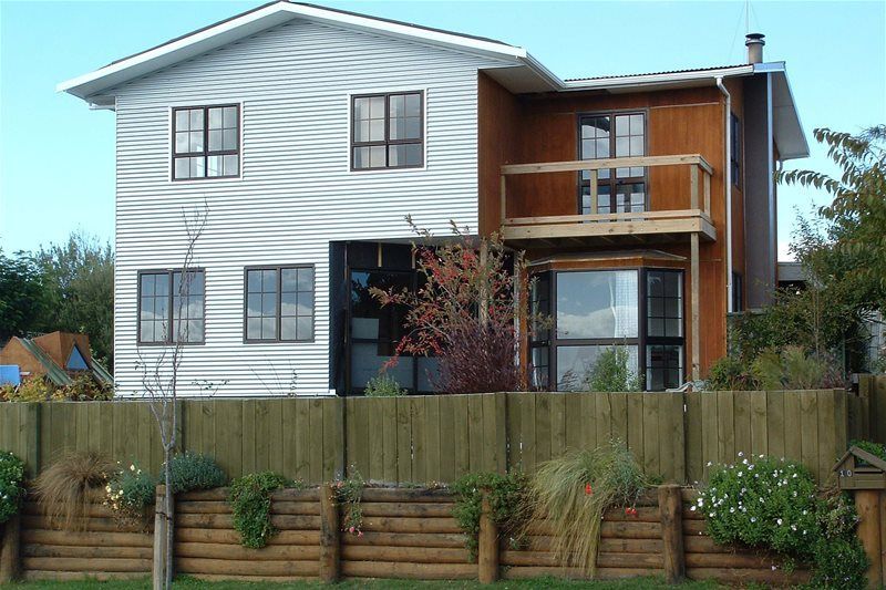 Two-story white house with wood balcony and fenced front yard under a cloudy sky