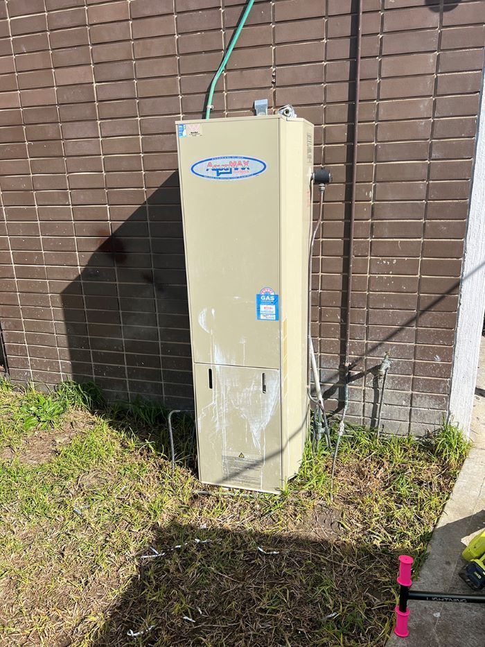 A Water Heater is Sitting in the Grass Next to a Brick Wall — Fig Facility Services in Bacchus Marsh, VIC