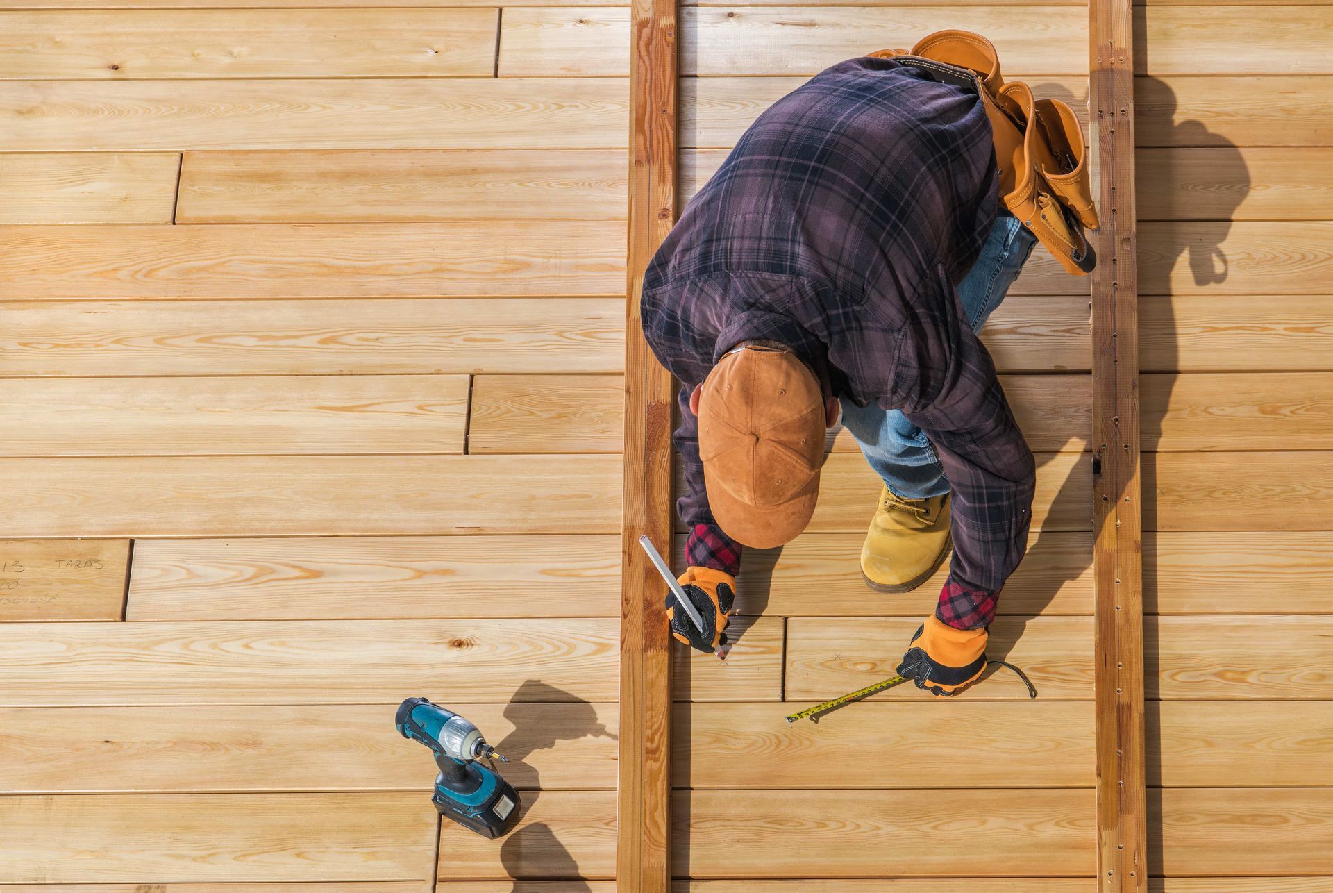 A man is working on a wooden deck with a drill and a tape measure.