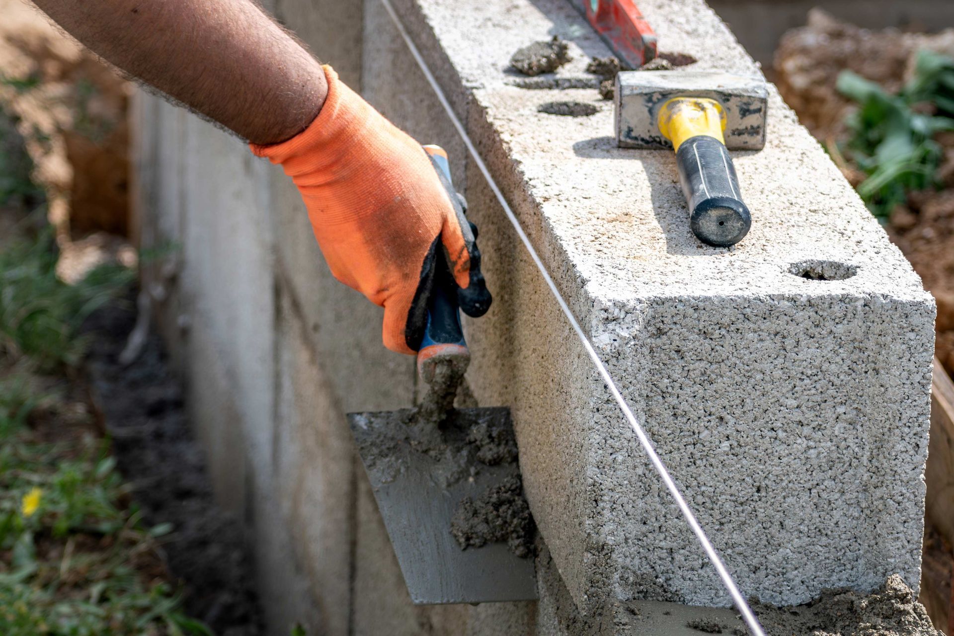 Person in orange glove uses trowel to spread mortar on concrete block wall. Person in orange glove uses trowel to spread mortar on concrete block wall.