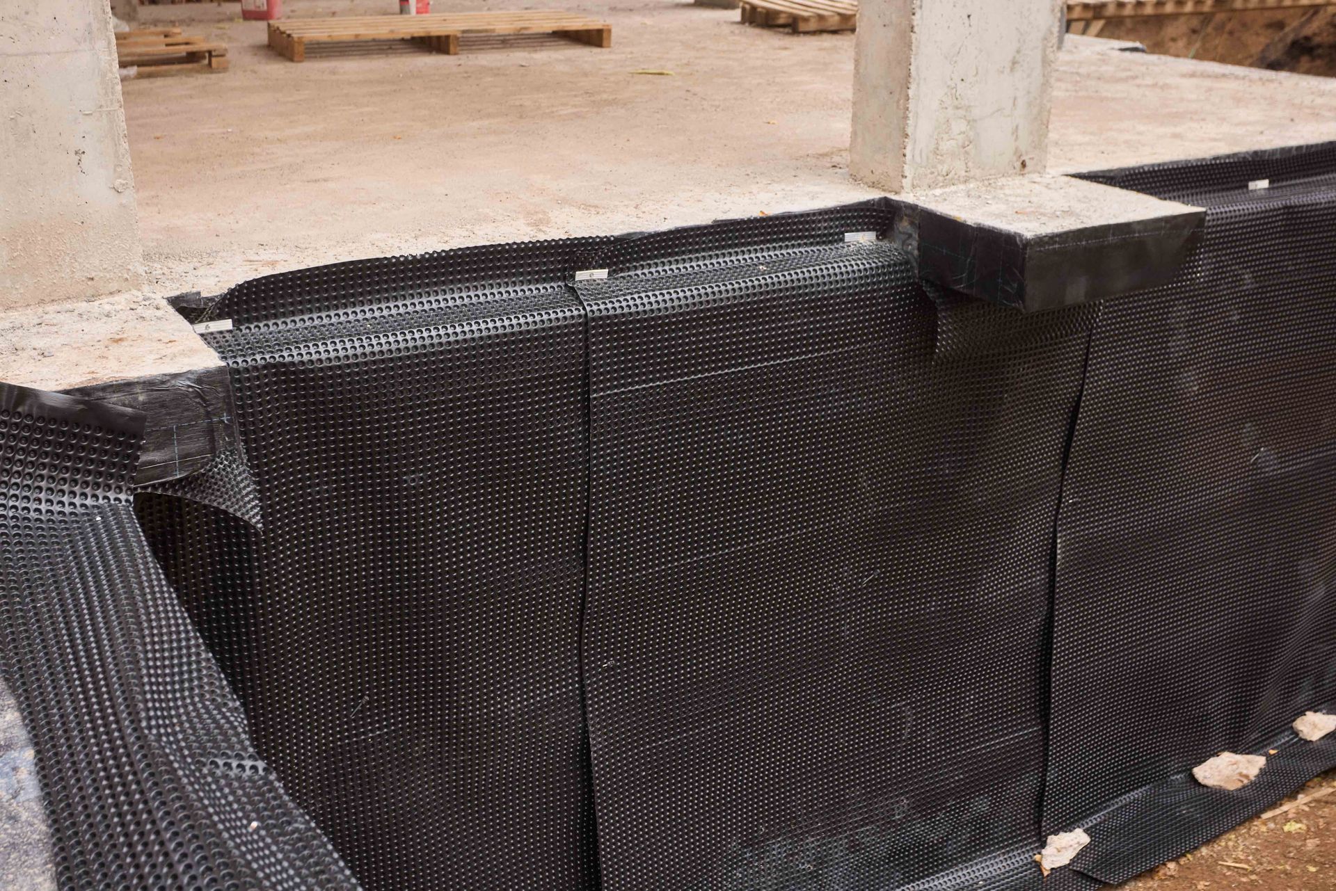 Black drainage membrane installed on a concrete foundation wall, construction site.