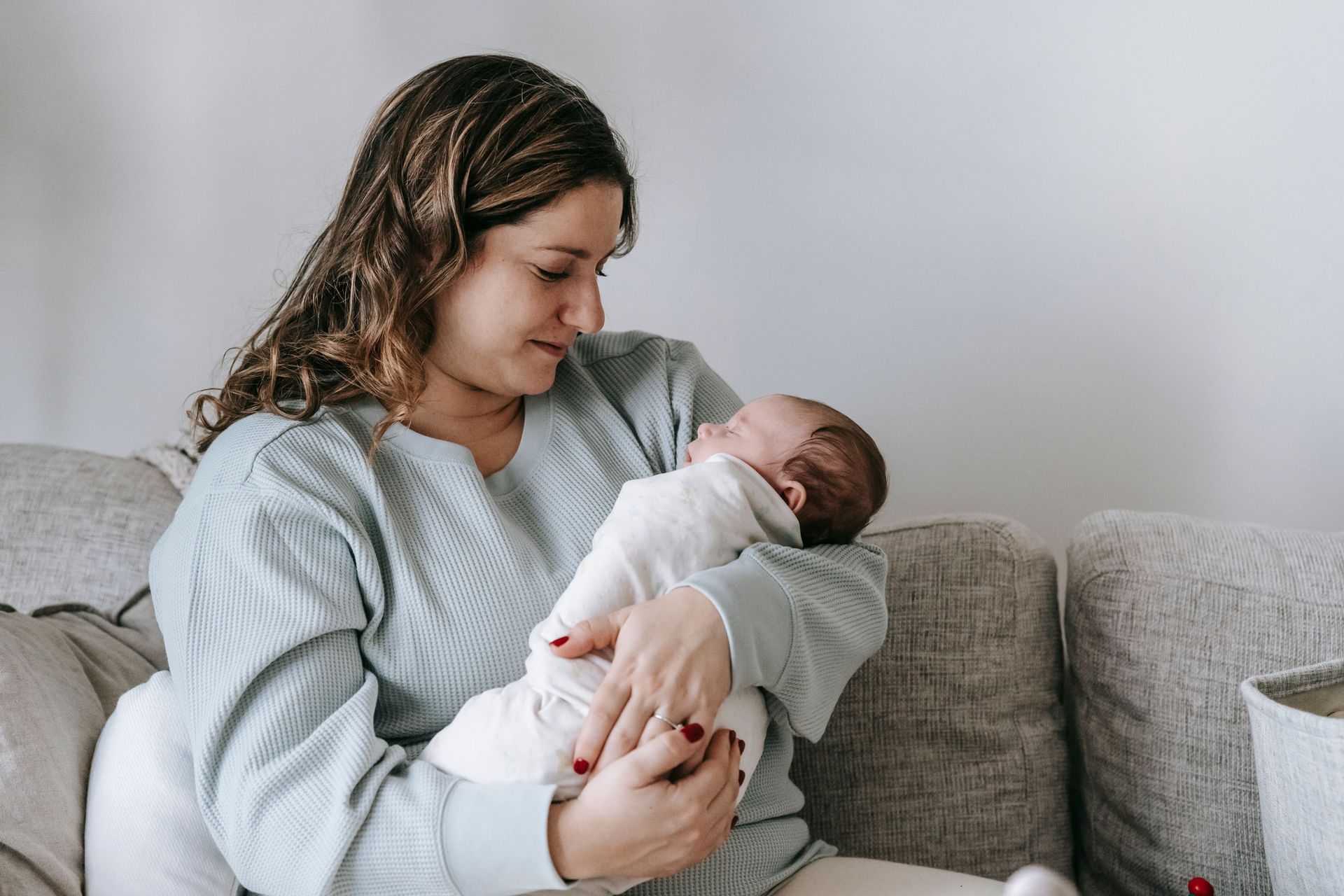 Person cradling a sleeping baby on a couch in a softly lit room