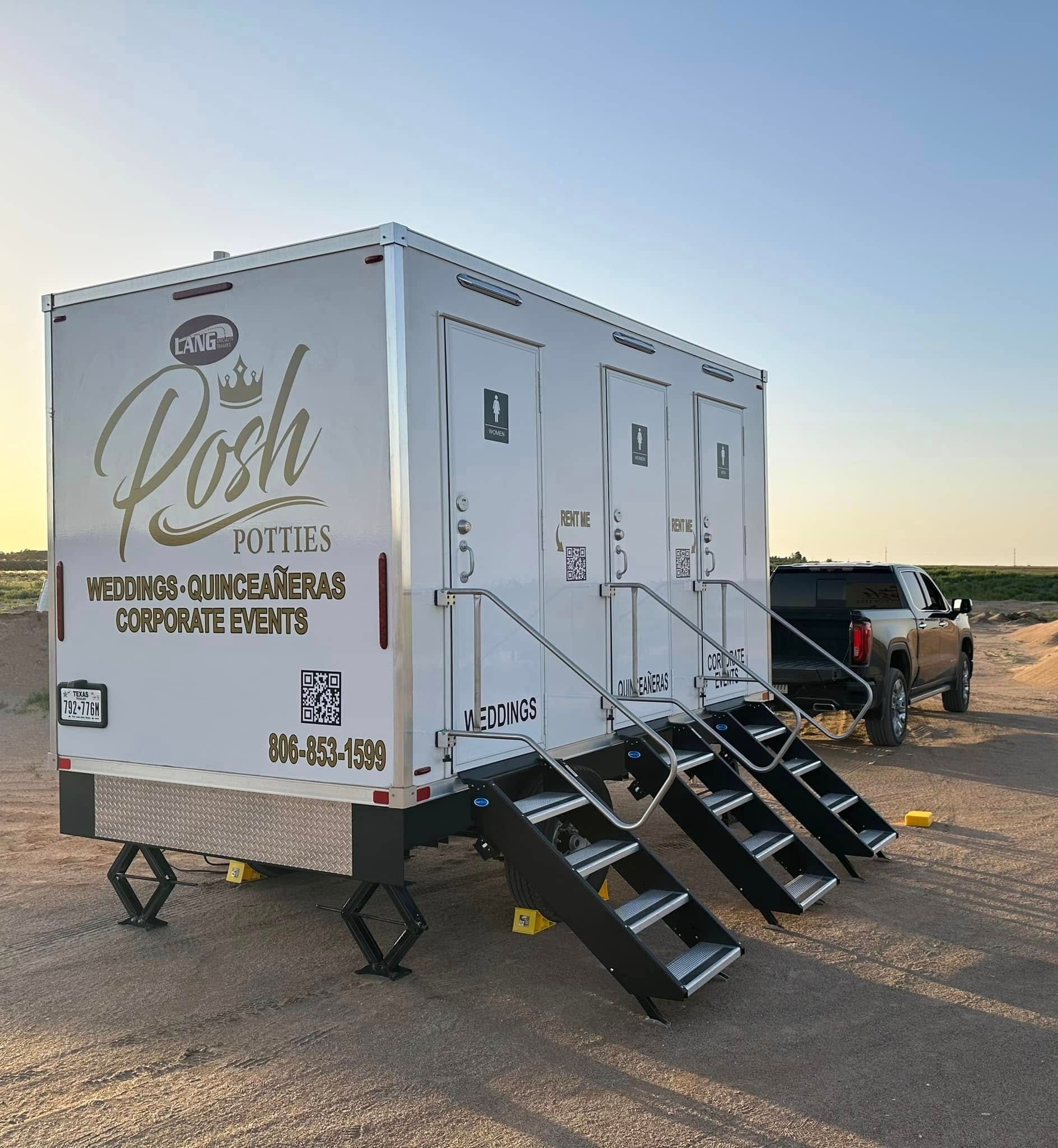White portable restroom trailer with three stalls, stairs, and a pickup truck. Desert setting.