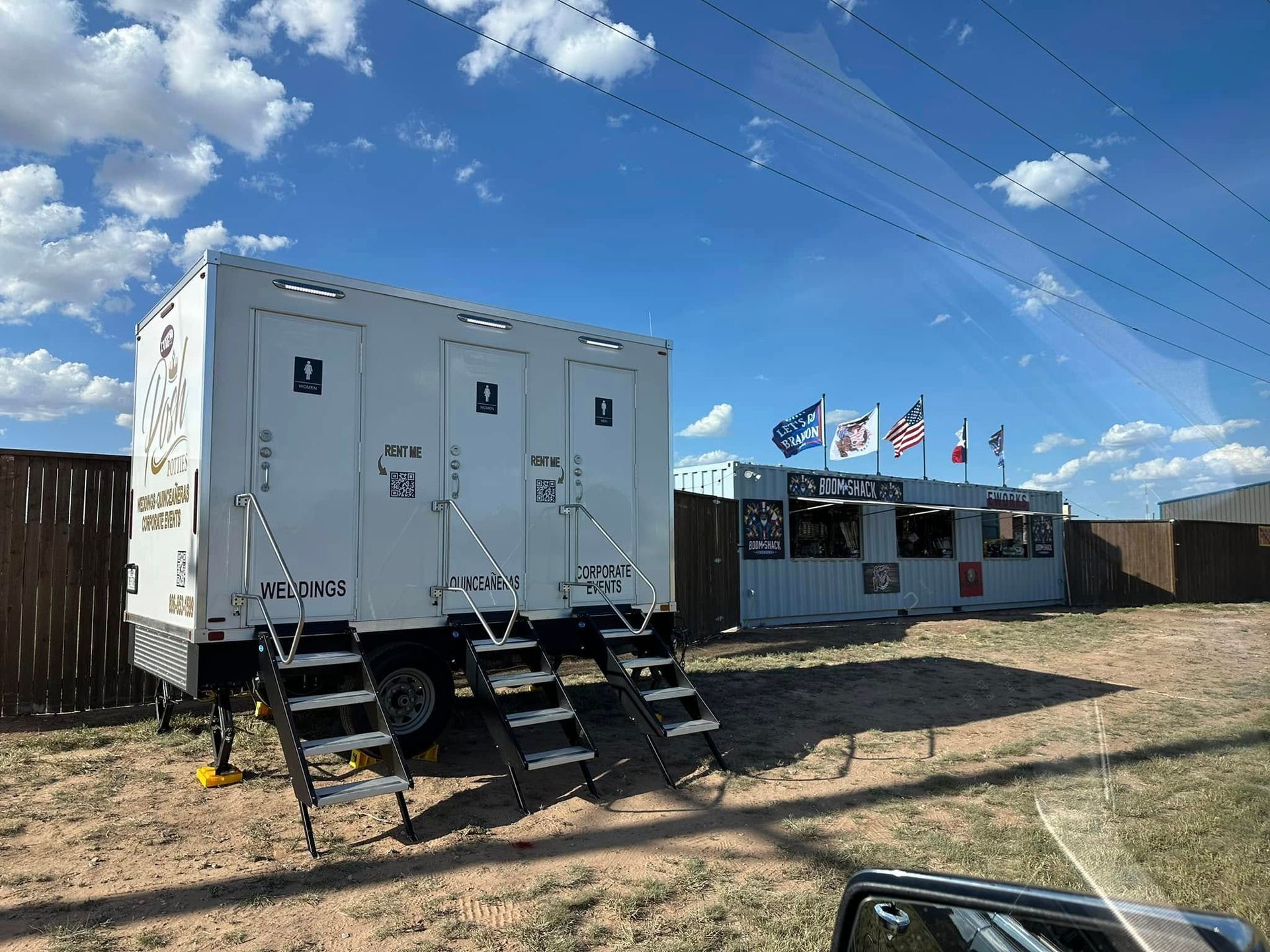 Portable toilets and a food stand on a grassy area under a blue sky with clouds.