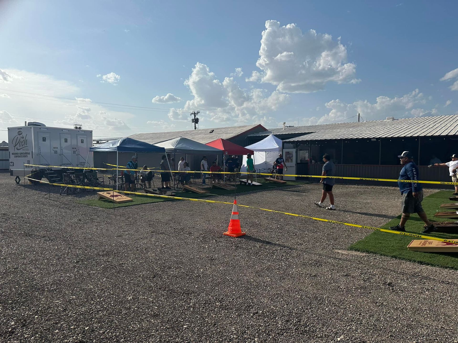 Outdoor event with tents, people, caution tape, and a gravel lot. Sunny day.