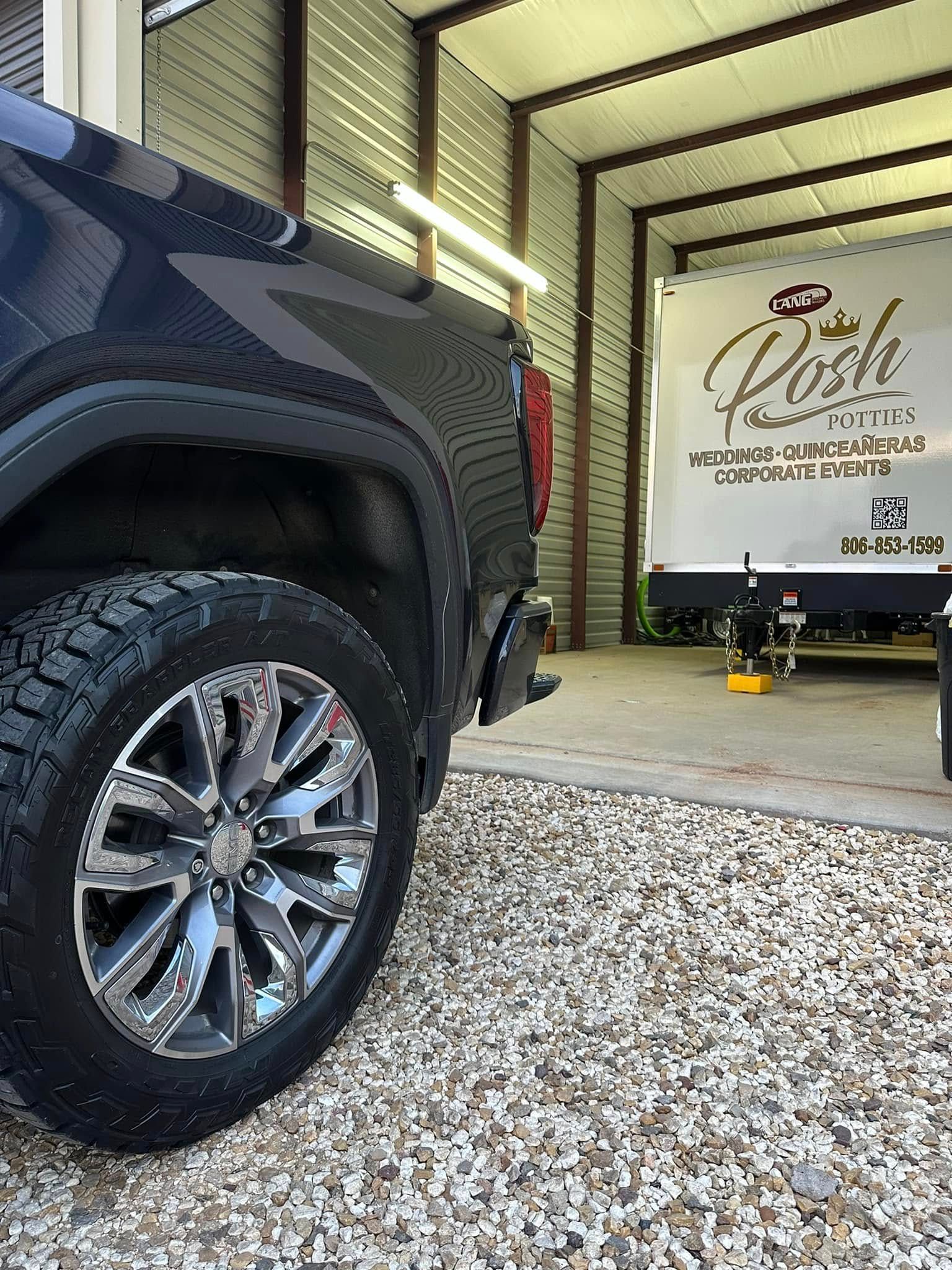Dark truck parked in gravel driveway near a trailer inside a metal shed.