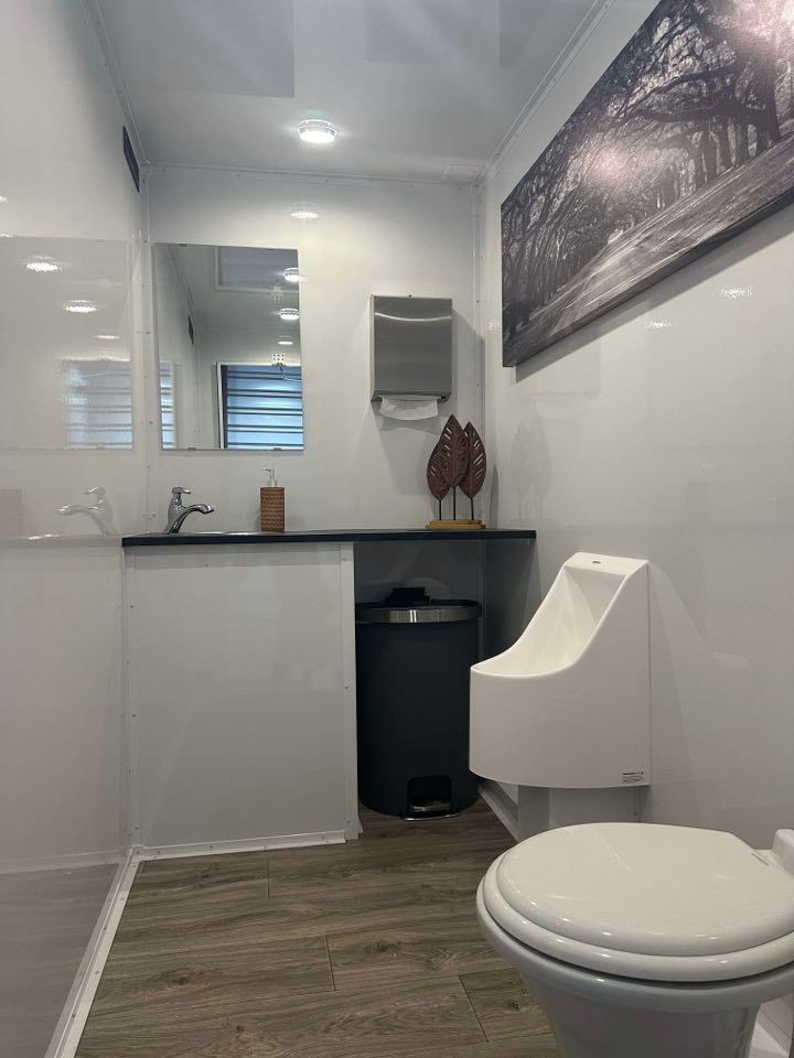 Interior of a clean, modern portable restroom with sink, toilet, and decorative artwork.