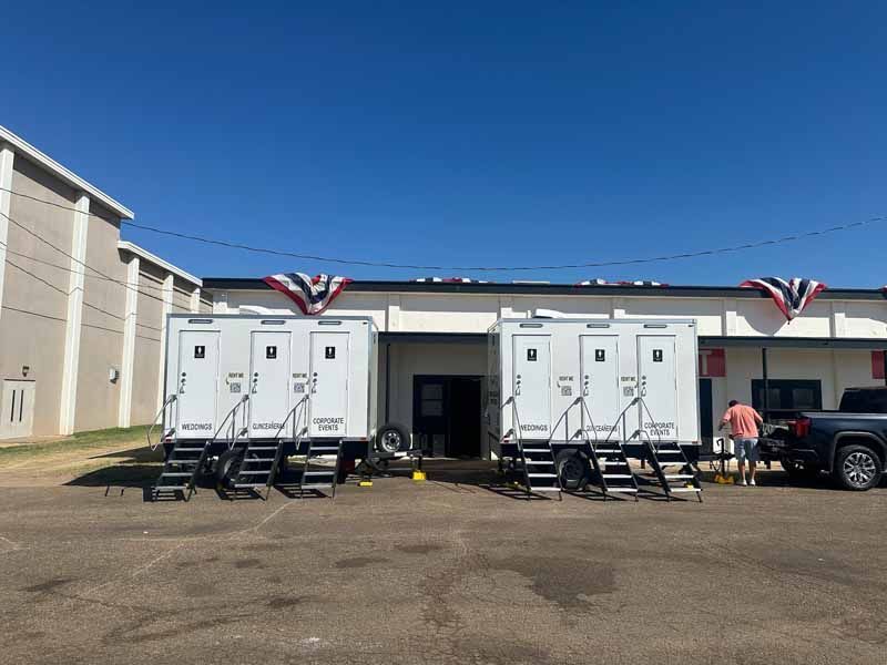 Two white portable restrooms with steps and banners, parked outside a building.