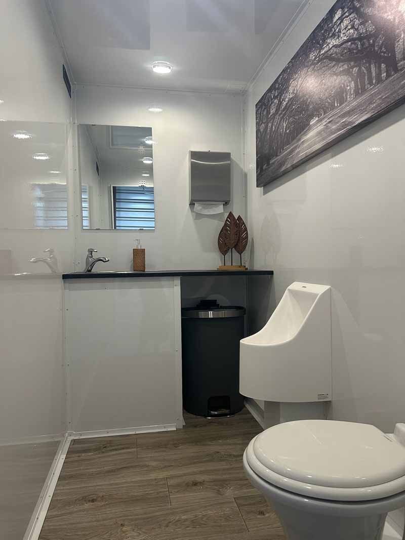 Modern restroom with white walls, sink, toilet, and trash can. Gray artwork hangs on the wall.