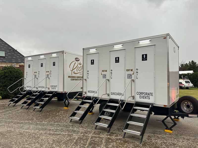 Two white portable restroom trailers with black steps, set up outdoors for a corporate event.