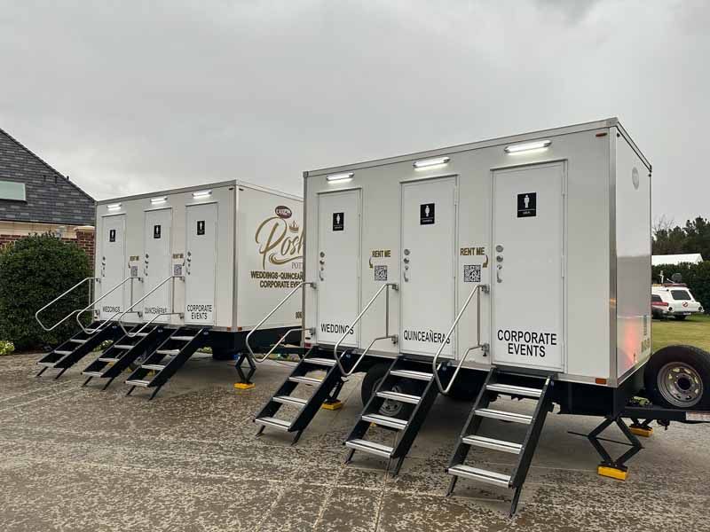 Two white portable restroom trailers with stairs, set up for an event.