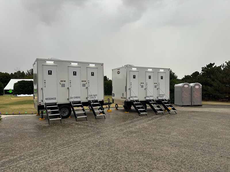 Two portable restroom trailers on a gray asphalt lot under an overcast sky.