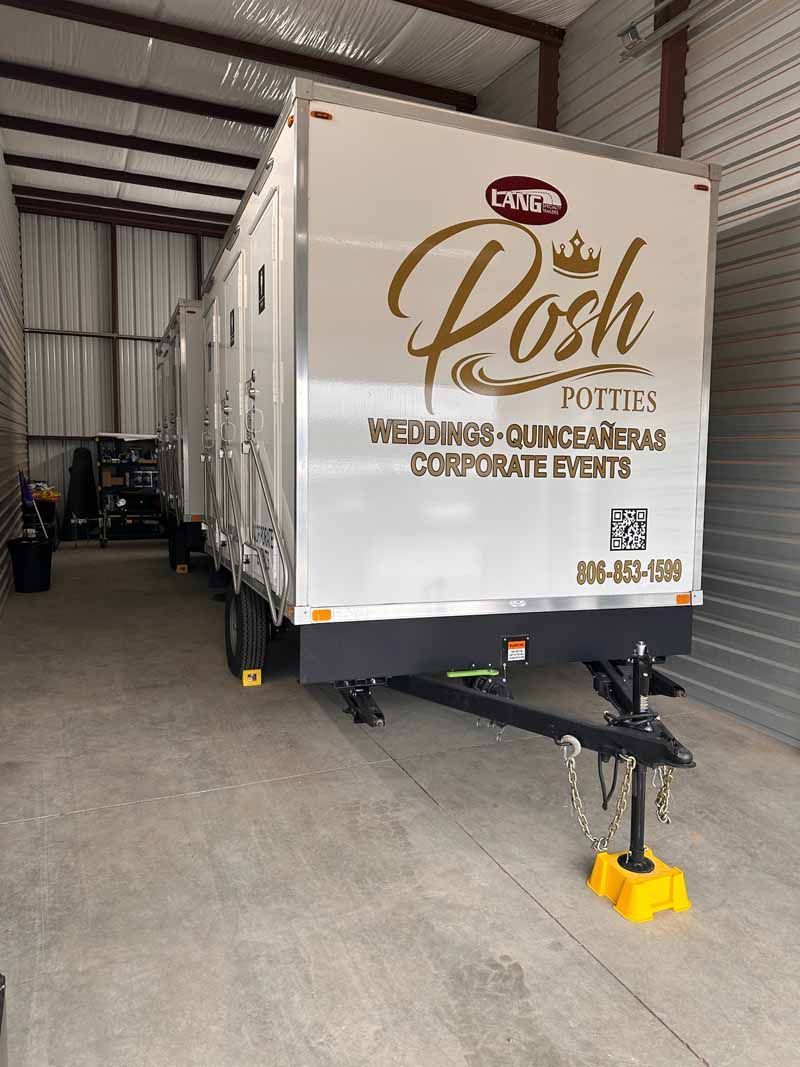 A white portable restroom trailer with gold lettering that reads 