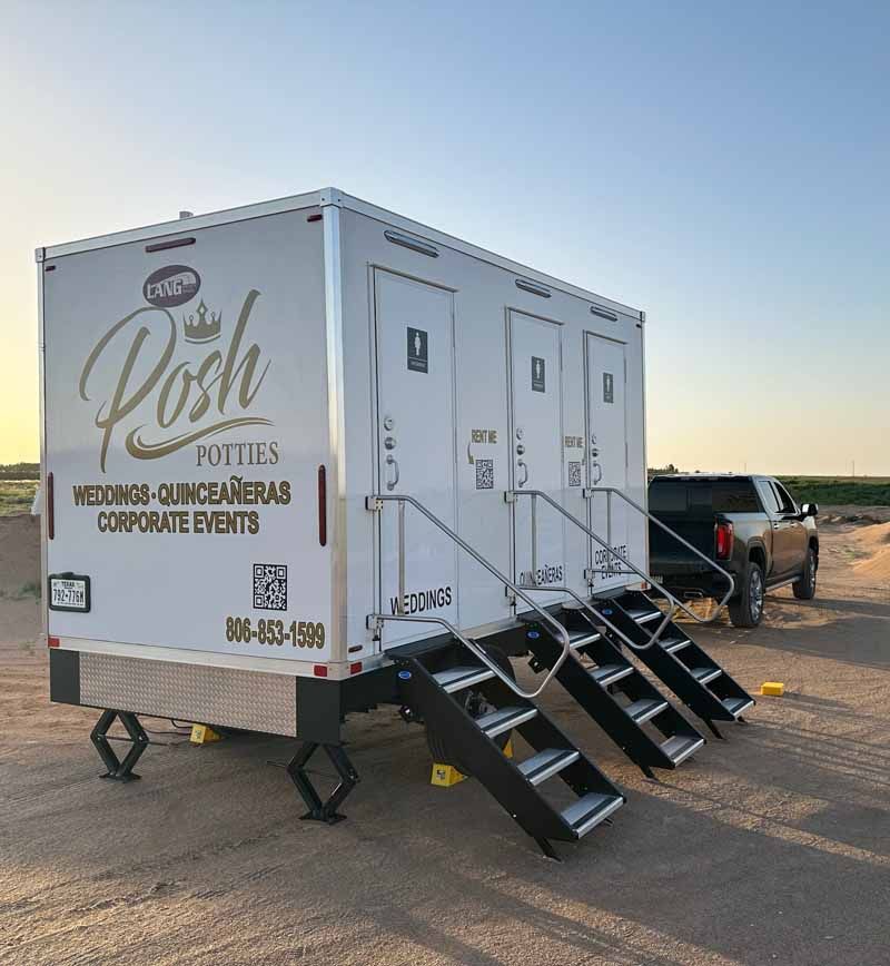 White portable restroom trailer with three stalls, stairs, and the words 