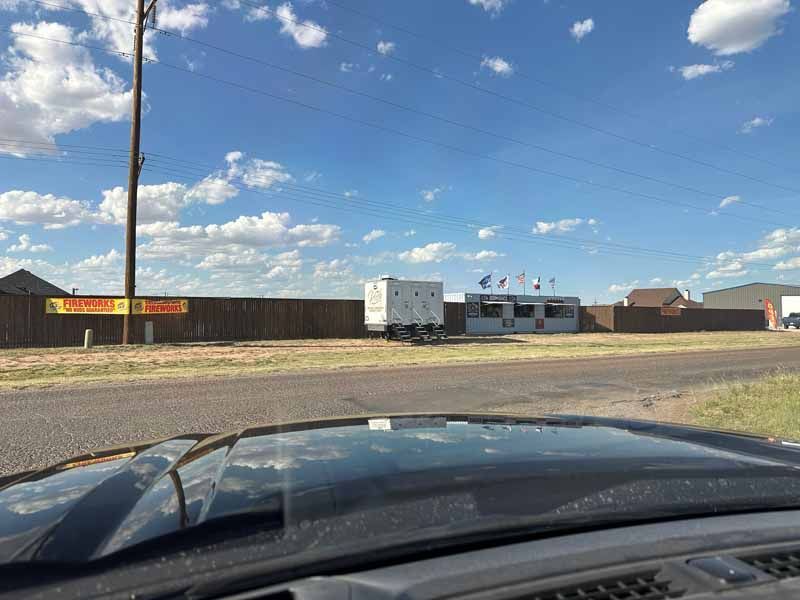 View from a vehicle's windshield; a trailer and brown fence sit roadside under a partly cloudy sky.
