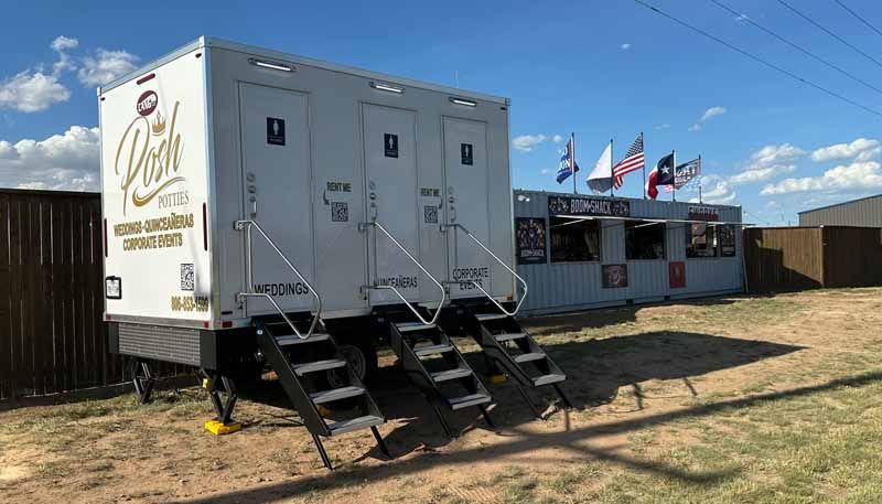 Portable restrooms with steps in front of a concession stand with American flags on display.