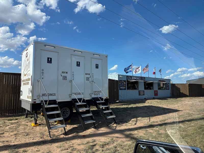 Portable toilets with steps and a food stand on a sunny day.