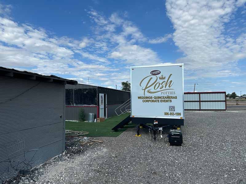Posh Potty trailer outside a building with a ramp, under a partly cloudy sky.