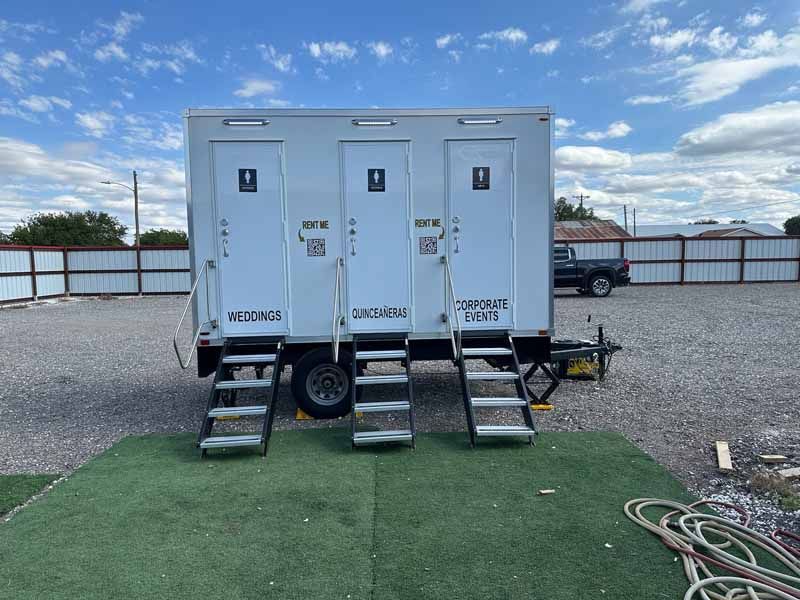 Portable restroom trailer with three stalls, white exterior, steps, and ramp for access.