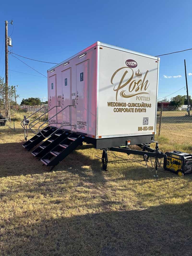 White portable restroom trailer with steps on grass under a blue sky; generator in foreground.