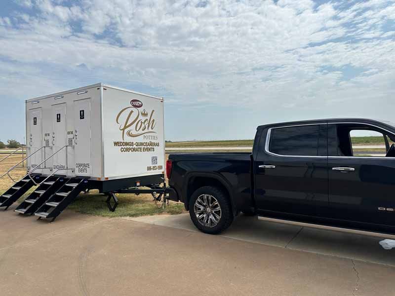 Black truck towing a portable restroom trailer labeled 