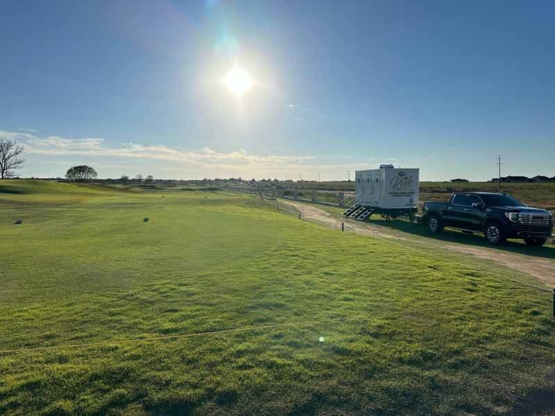 A truck towing a trailer on a grassy field under a bright sun.
