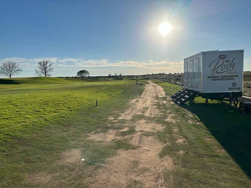 A golf course with a dirt path leading to a white trailer under a bright sun.