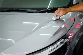 A person is polishing the hood of a car with a sponge.