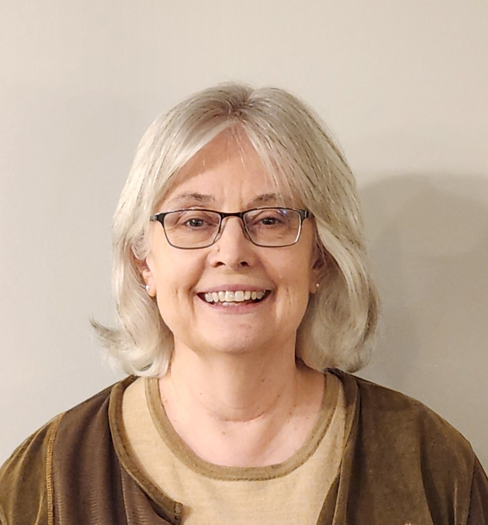A woman wearing glasses and a brown sweater is smiling for the camera.