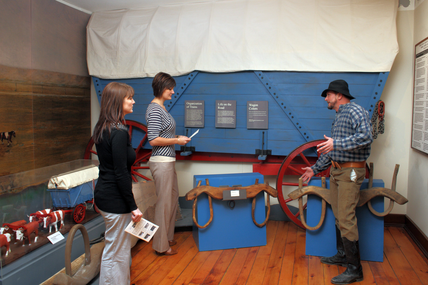 A man and two women are looking at a wagon wheel in a museum