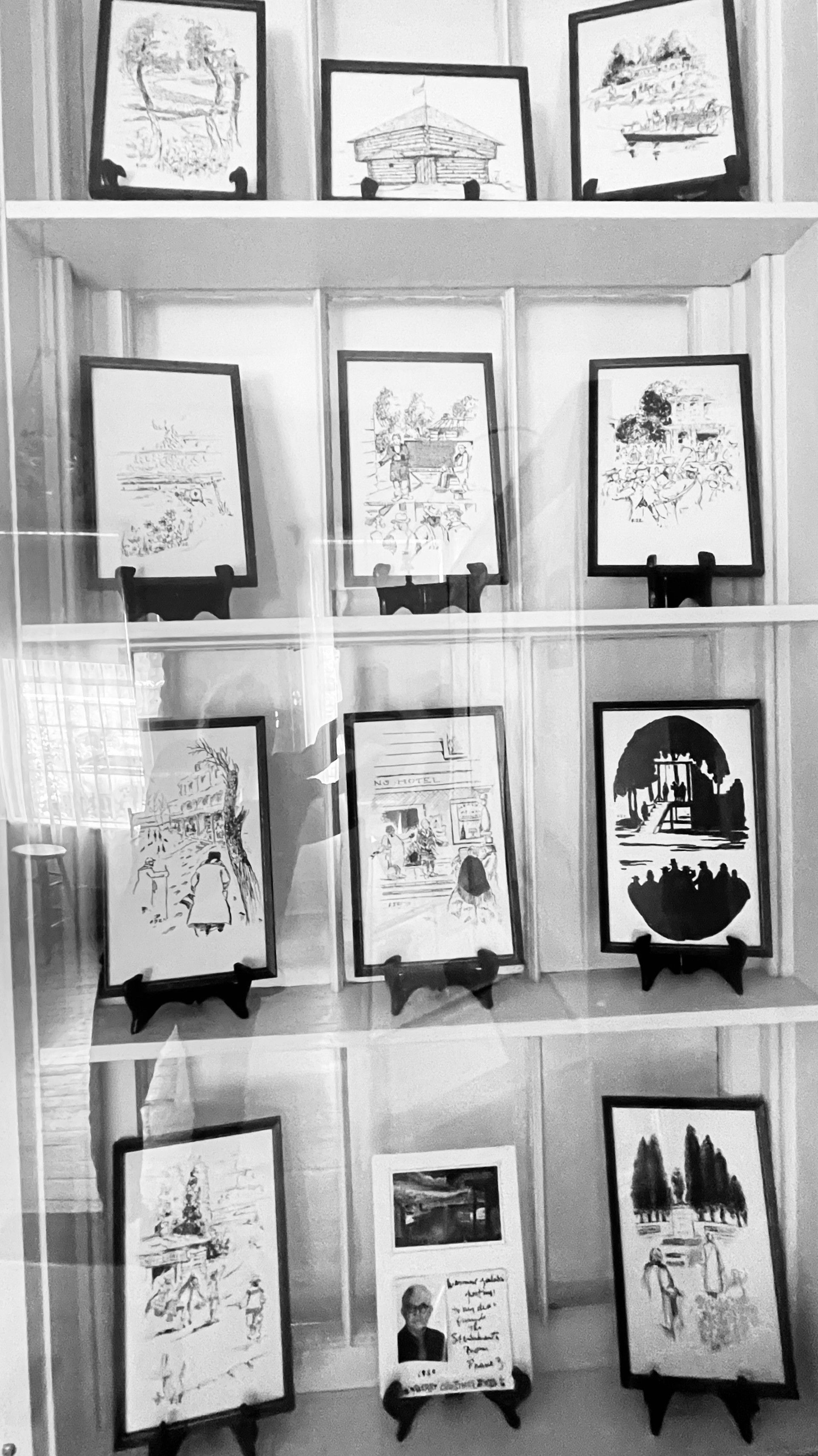 A black and white photo of a display case filled with paintings.