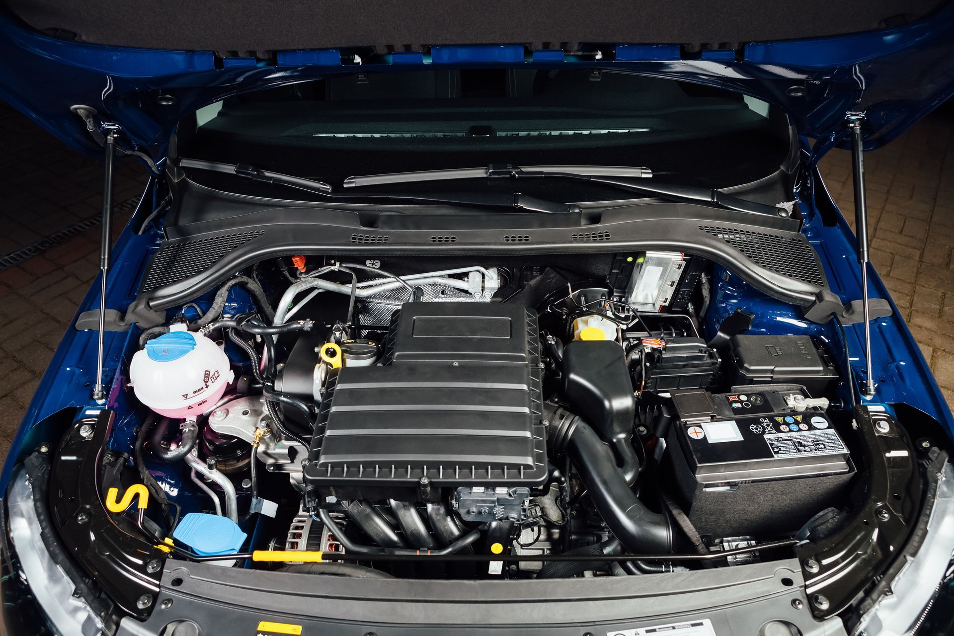 Car engine bay with hood open, showing a black intake cover and blue coolant reservoir in a garage | LTI Automotive