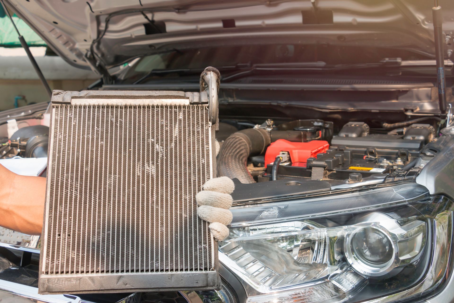 Mechanic holding a dirty car radiator in front of an open engine bay | LTI Automotive
