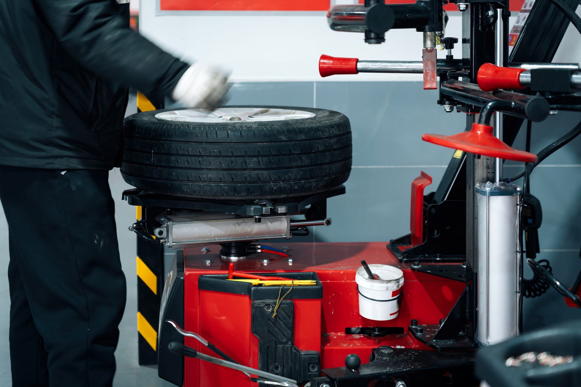 Mechanic changing a car tire beside a red wheel balancer in a garage | LTI Automotive
