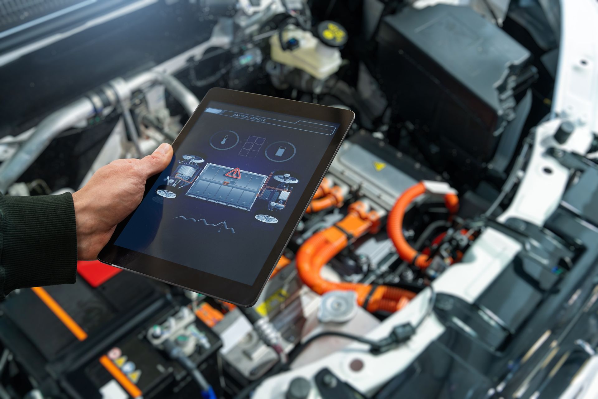 Hand holding a tablet showing vehicle diagnostics beside an electric car engine compartment | LTI Automotive