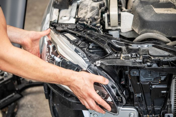 Hands fitting a car's front bumper and headlight assembly during repair | LTI Automotive