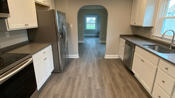 A kitchen with white cabinets , stainless steel appliances , a refrigerator and a sink.
