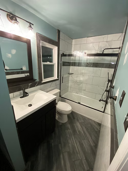 A bathroom with a toilet , sink , shower and window.